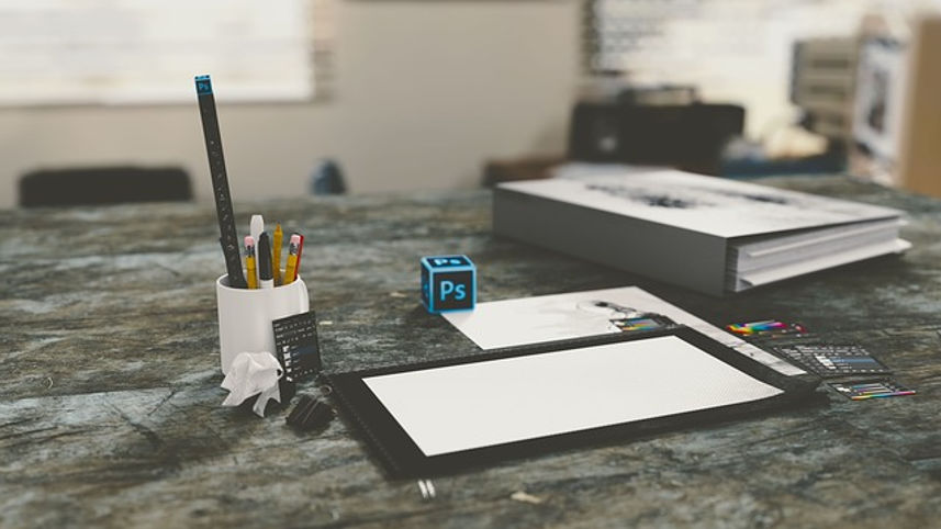 Photoshop logo cube near a white canvas on a desk